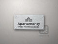 Srebrny szyld z grafiką Łodzi i napisem Apartamenty przy piotrkowskiej