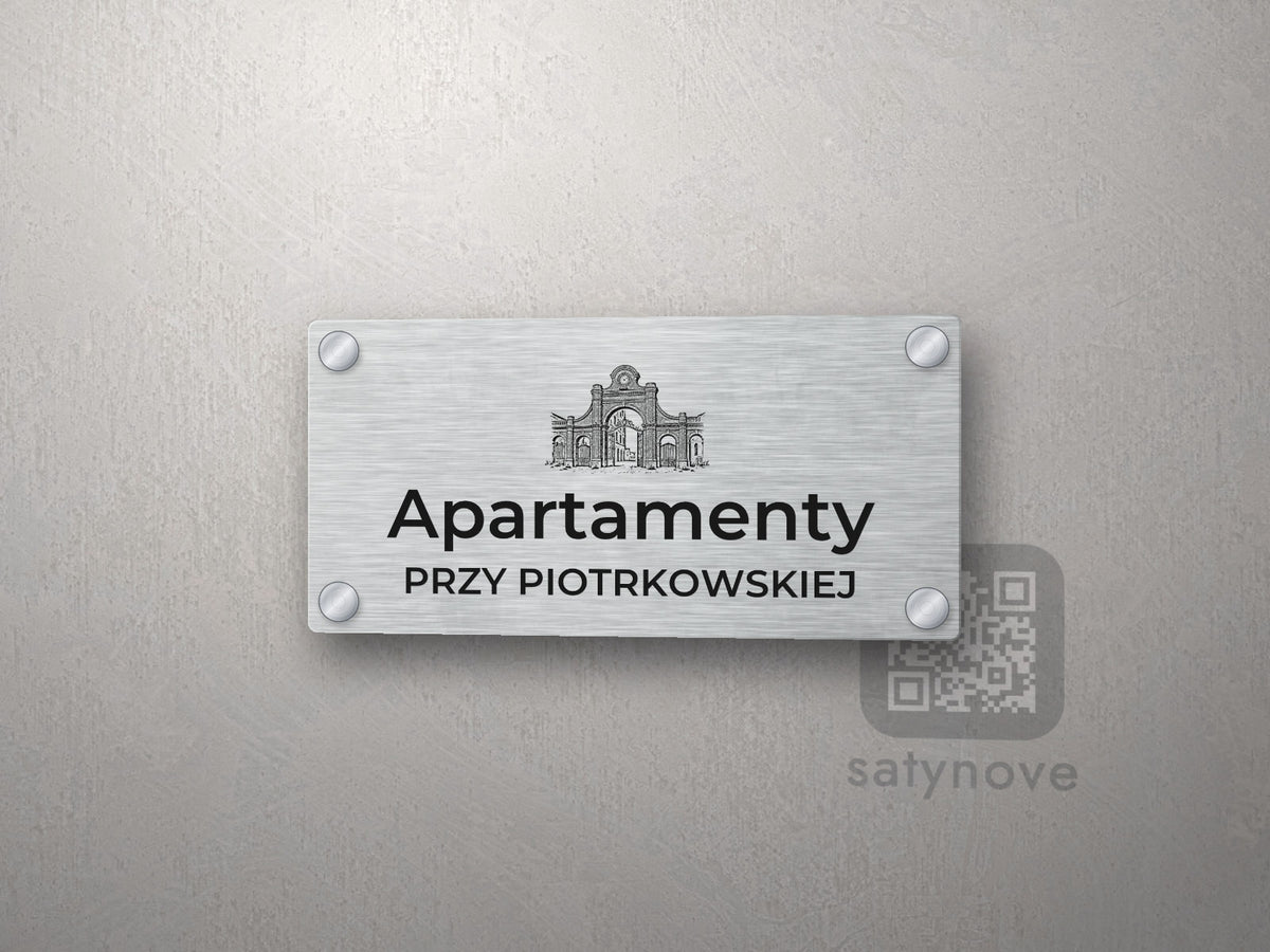 Srebrny szyld z grafiką Łodzi i napisem Apartamenty przy piotrkowskiej