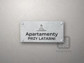 Srebrny szyld z grafiką Kołobrzegu i napisem Apartamenty przy latarni