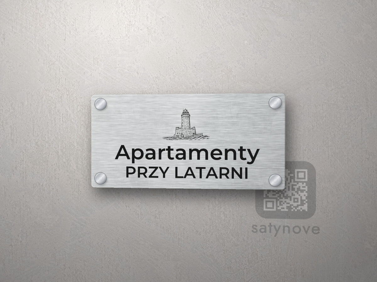 Srebrny szyld z grafiką Kołobrzegu i napisem Apartamenty przy latarni