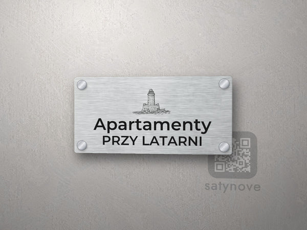 Srebrny szyld z grafiką Kołobrzegu i napisem Apartamenty przy latarni