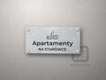 Srebrny szyld z grafiką Warszawy i napisem Apartamenty na starówce