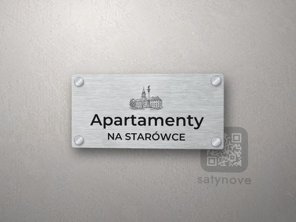 Srebrny szyld z grafiką Warszawy i napisem Apartamenty na starówce