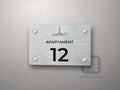 Srebrna tabliczka z numerem apartamentu 12 i grafiką Wybrzeża Rewalskiego