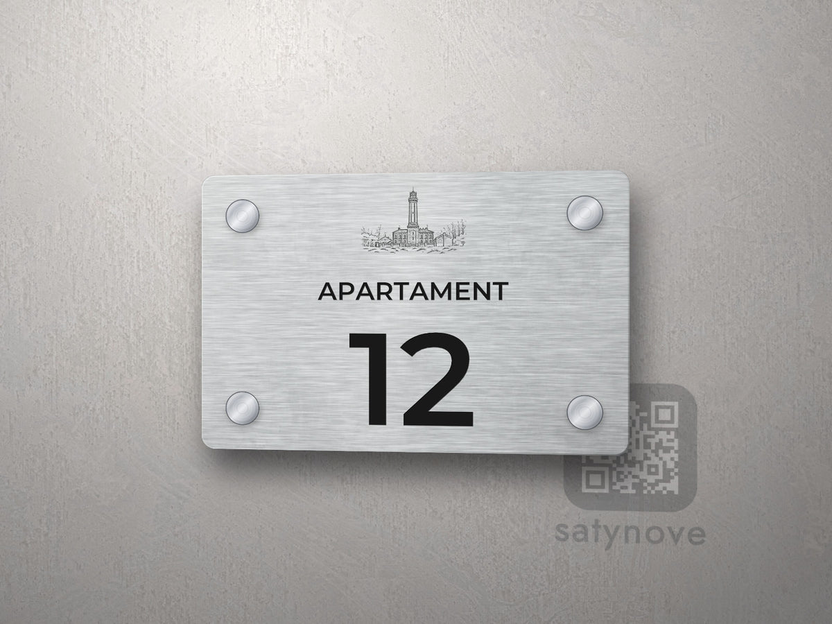 Srebrna tabliczka z numerem apartamentu 12 i grafiką Wybrzeża Rewalskiego