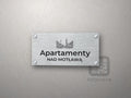 Srebrny szyld z grafiką Trójmiasta i napisem Apartamenty nad motławą