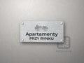 Srebrny szyld z grafiką Krakowa i napisem Apartamenty przy rynku