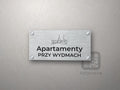 Srebrny szyld z grafiką Łeby i napisem Apartamenty przy wydmach