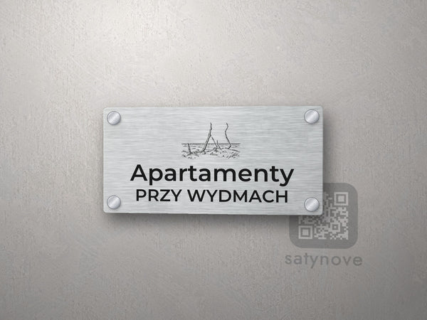 Srebrny szyld z grafiką Łeby i napisem Apartamenty przy wydmach