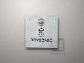 Srebrna tabliczka Prysznic z logo schroniska u góry, piktogramem i podpisem PRYSZNIC