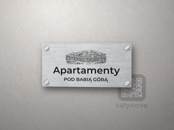 Srebrny szyld z grafiką Beskidów i napisem Apartamenty pod babią górą