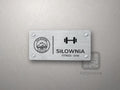 Pozioma tabliczka z logo schroniska, linią, hantlą nad podpisem SIŁOWNIA