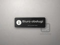 Mała czarna tabliczka z symbolem informacji i napisem „Biuro obsługi”