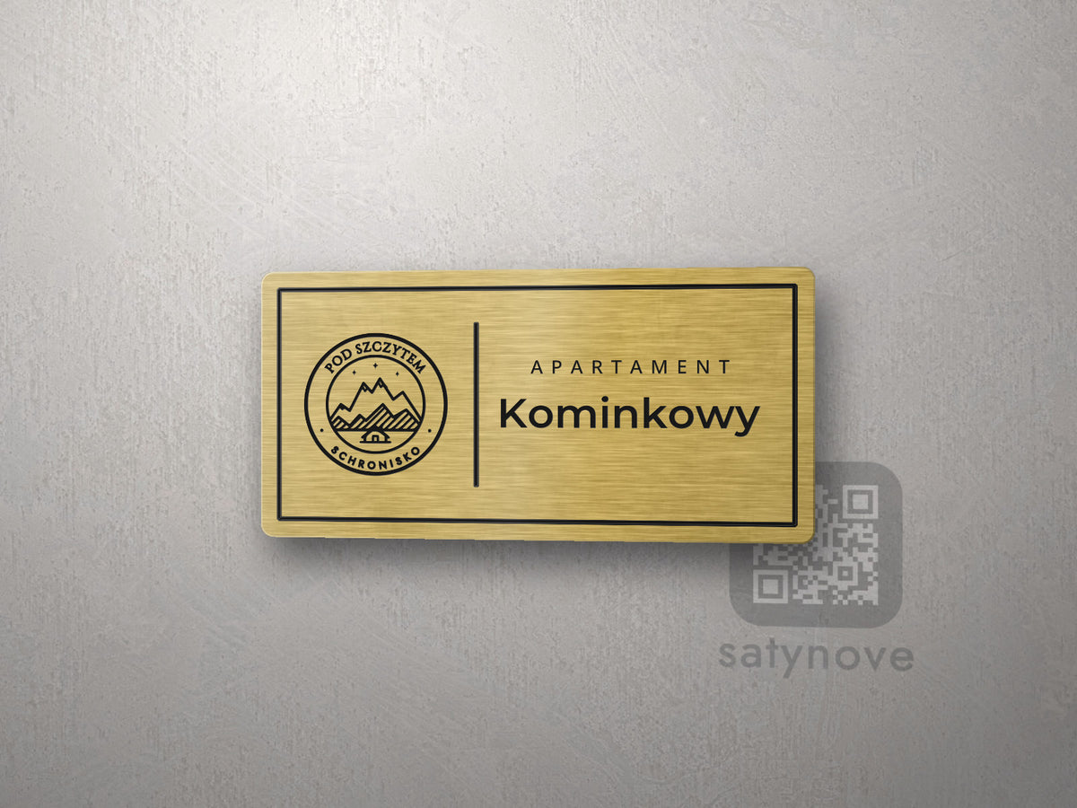 Złota tabliczka apartamentu w ramce z logo schroniska i nazwą Kominkowy