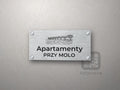 Srebrny szyld z grafiką Międzyzdrojów i Świnoujścia i napisem Apartamenty przy molo