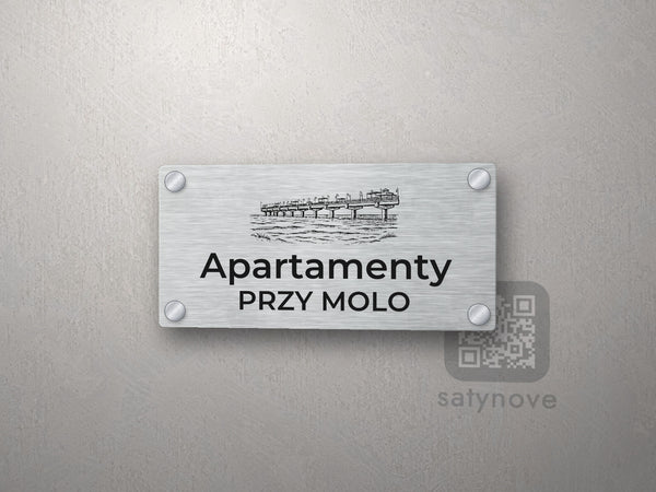 Srebrny szyld z grafiką Międzyzdrojów i Świnoujścia i napisem Apartamenty przy molo