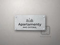Srebrny szyld z grafiką Półwyspu Helskiego i napisem Apartamenty nad zatoką