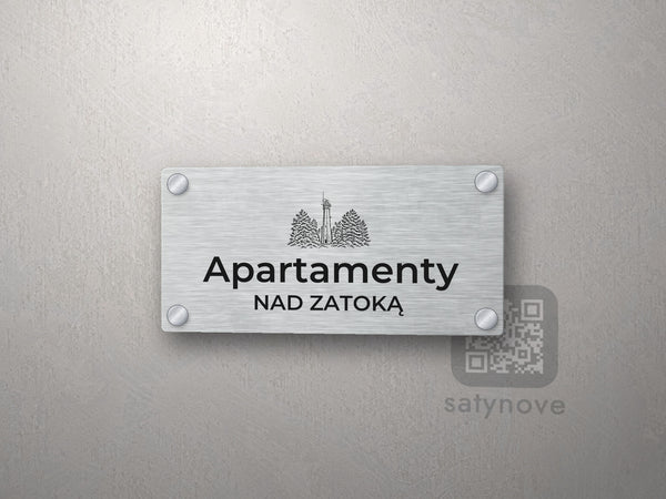 Srebrny szyld z grafiką Półwyspu Helskiego i napisem Apartamenty nad zatoką