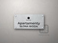 Srebrny szyld z logo obiektu i napisem Apartamenty Słona Woda