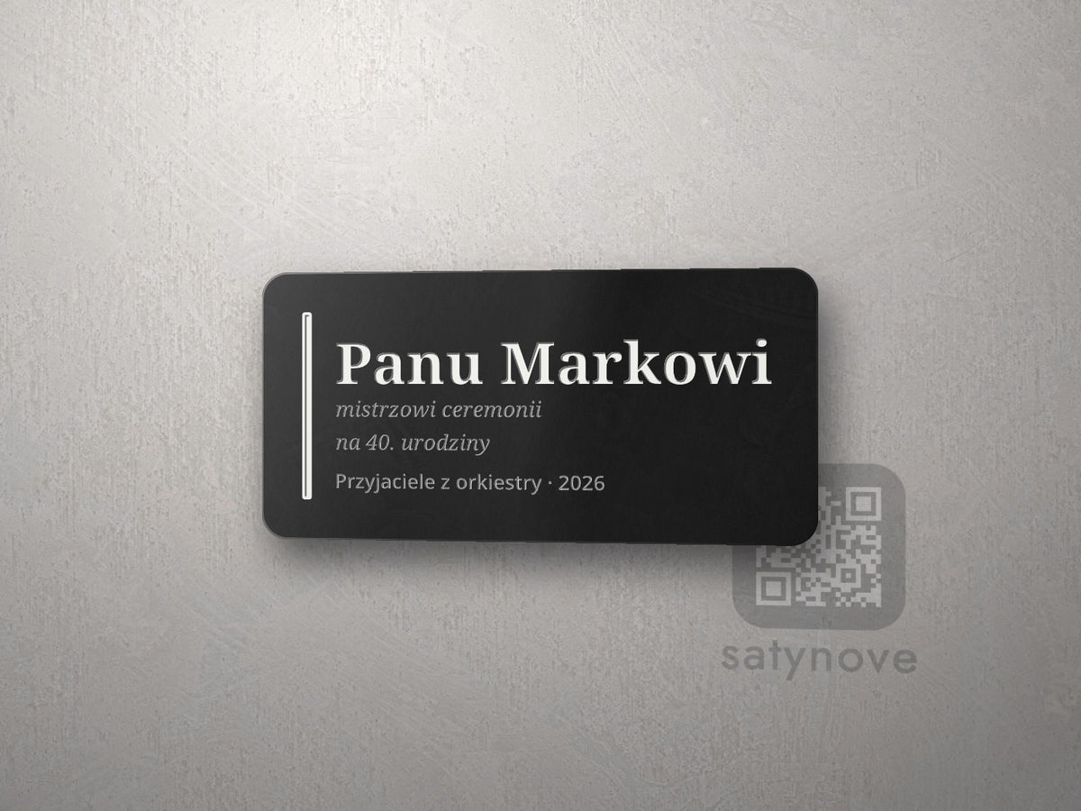 Czarna tabliczka z białym grawerem: pionowa linia, „Panu Markowi”, dedykacja i podpis