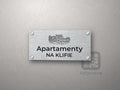 Srebrny szyld z grafiką Wybrzeża Rewalskiego i napisem Apartamenty na klifie