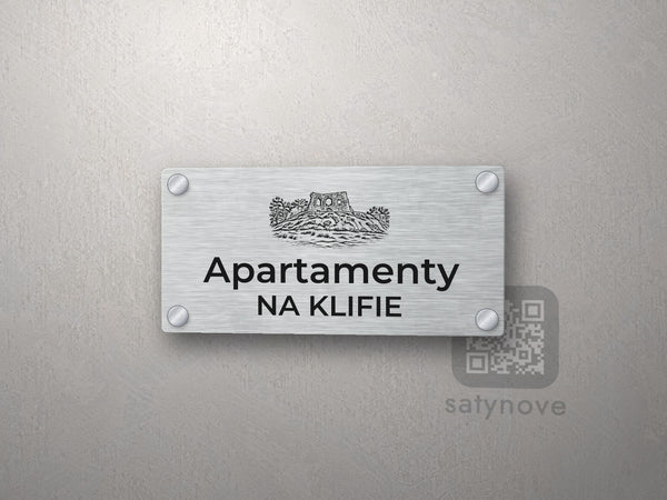 Srebrny szyld z grafiką Wybrzeża Rewalskiego i napisem Apartamenty na klifie