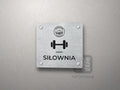 Srebrna tabliczka Siłownia z logo schroniska u góry, piktogramem i podpisem SIŁOWNIA