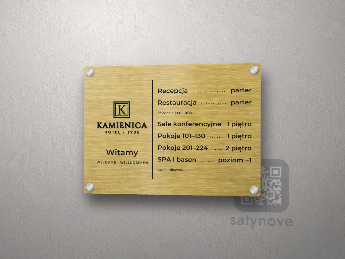 Złota tablica recepcji z logo Kamienica, napisem Witamy i spisem pięter z kropkami