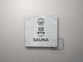 Srebrna tabliczka Sauna z logo schroniska u góry, piktogramem i podpisem SAUNA