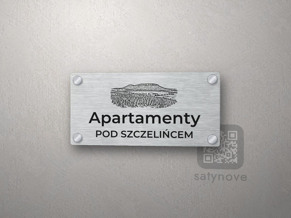Srebrny szyld z grafiką Gór Stołowych i napisem Apartamenty pod szczelińcem