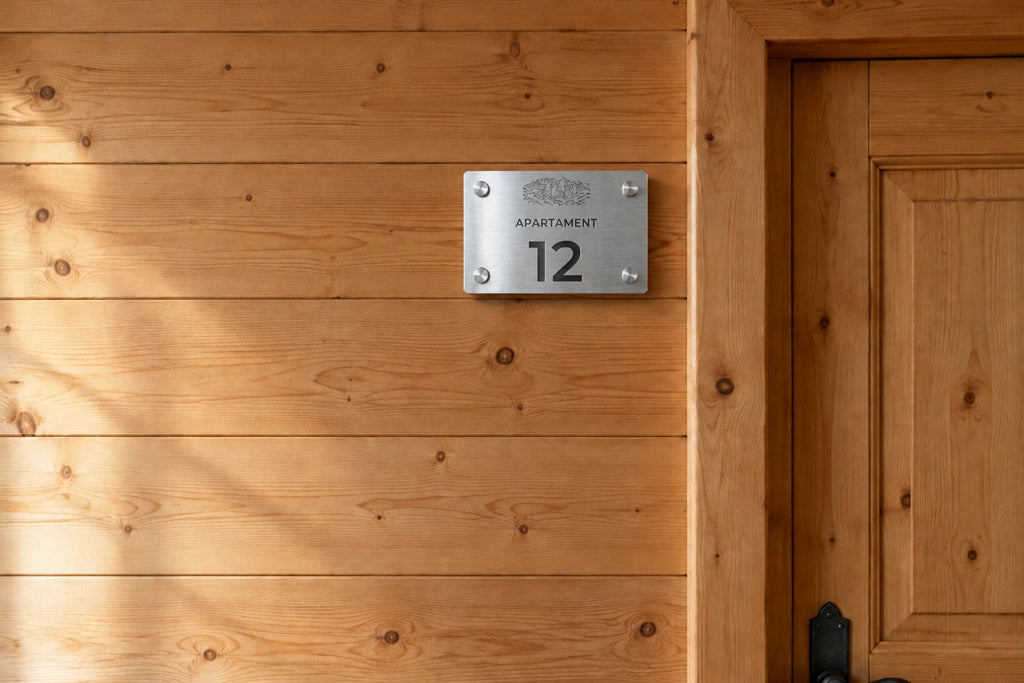 Grawerowana tabliczka z numerem apartamentu i grafiką Tatr na drewnianej ścianie pensjonatu